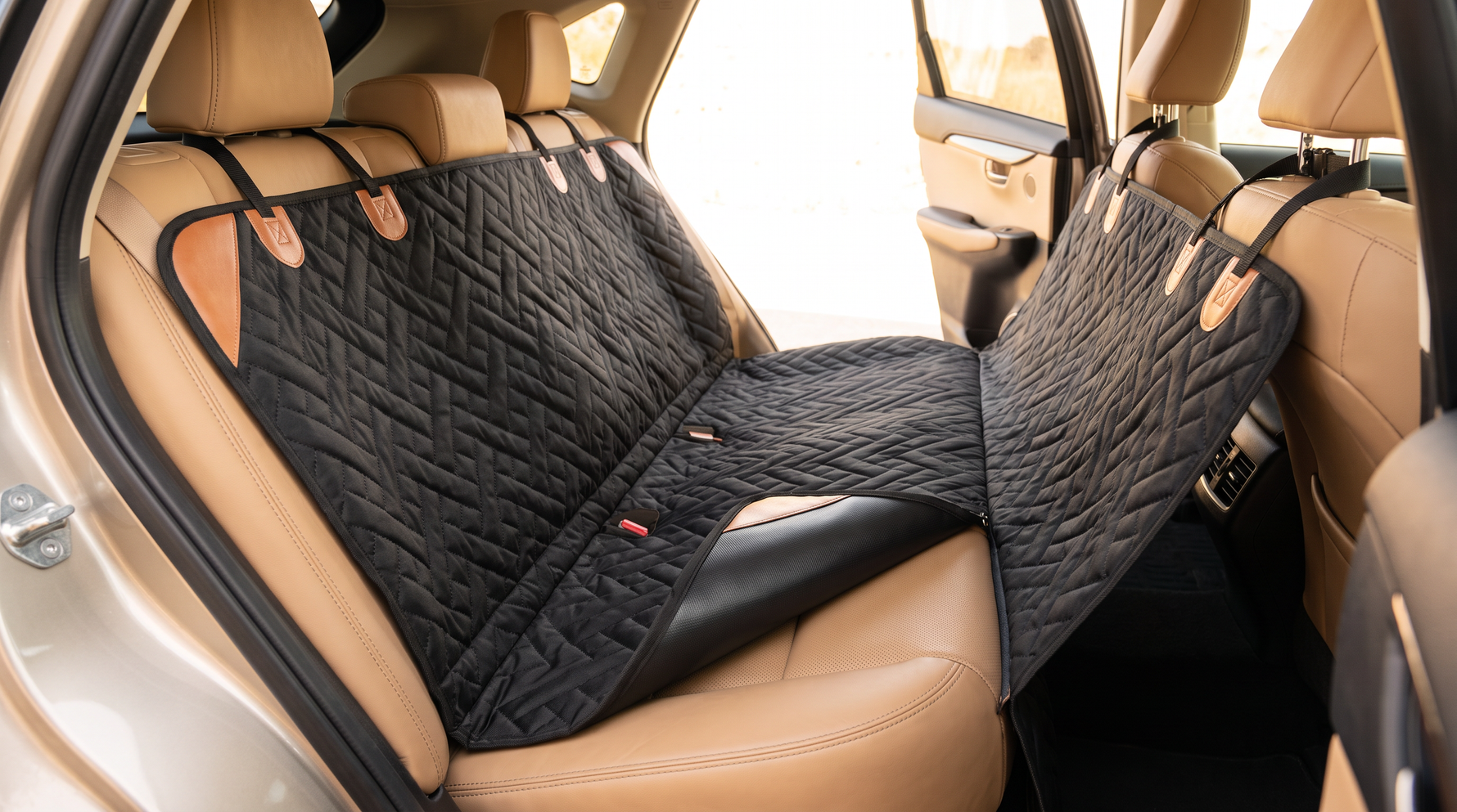 A dog seat cover laid over a tan leather back seat with one corner lifted