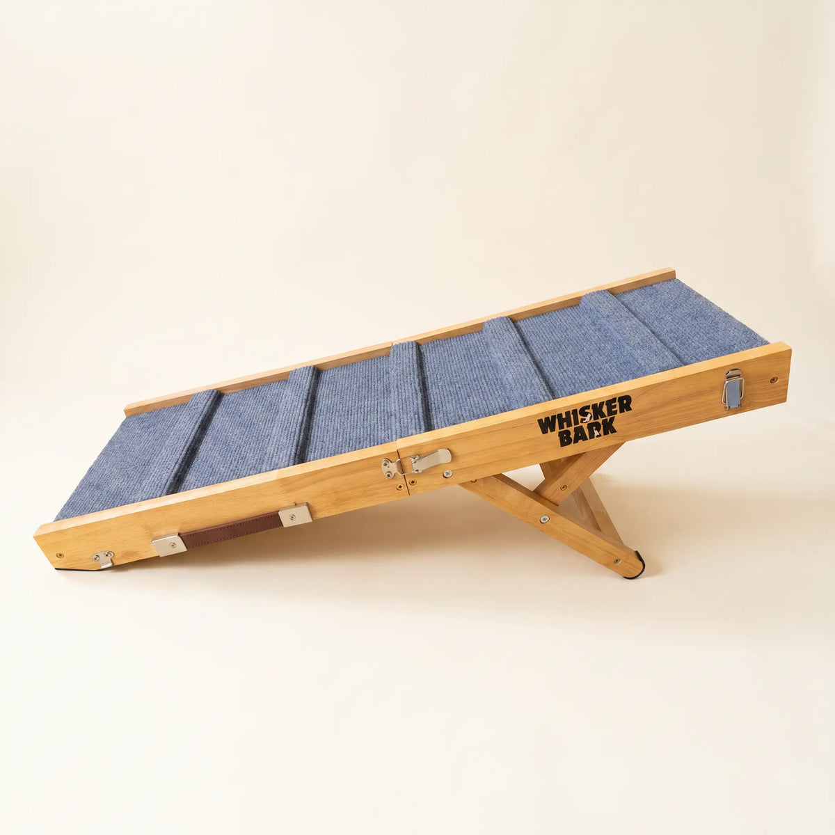 Whisker Bark folding dog ramp set up at an angle on a cream background, showing the natural wood frame and grey-blue carpet deck.
